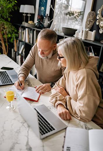 A senior couple reviews their checklist as they go through an estate planning quiz on their laptop.