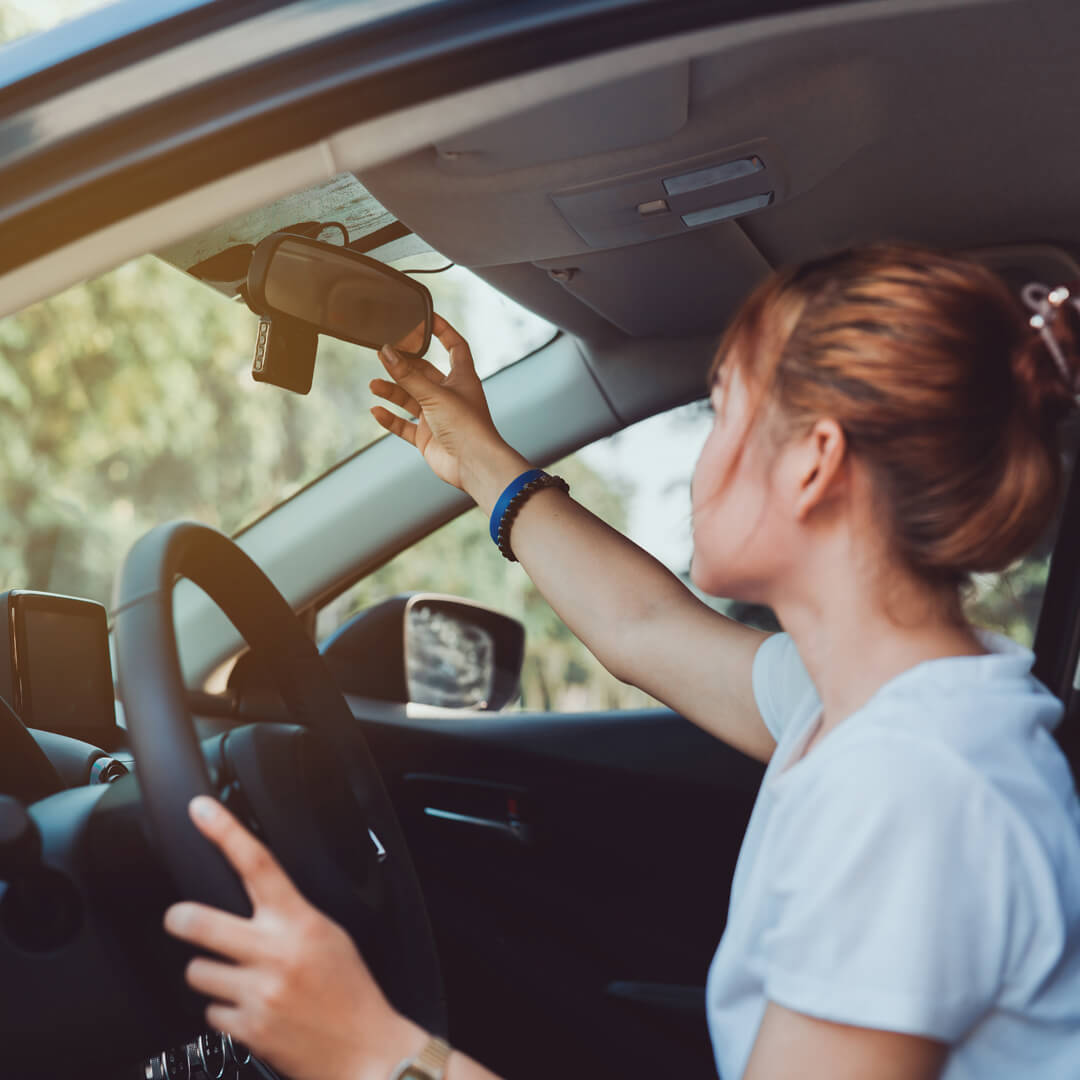 Young woman in her car, adjusting her rearview mirror and practicing defensive driving.