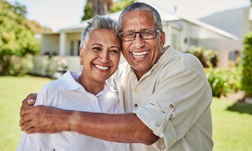 Older smiling couple standing outside a 55+ community home.