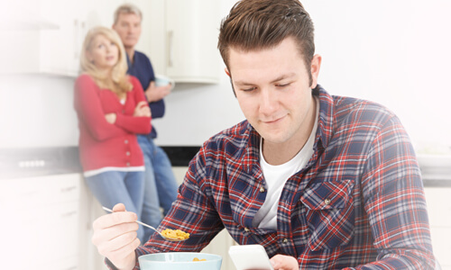 Grown man eating cereal at parents' kitchen table, parents looking at him with concern.