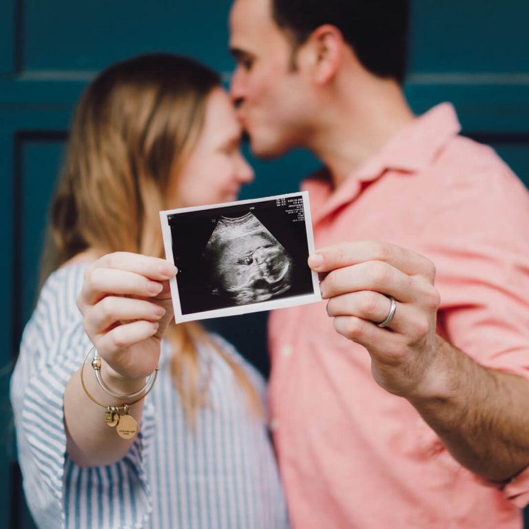 Expectant couple holding out sonogram image of new baby towards camera.