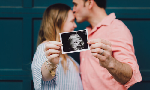 Expectant couple holding out sonogram image of new baby towards camera.
