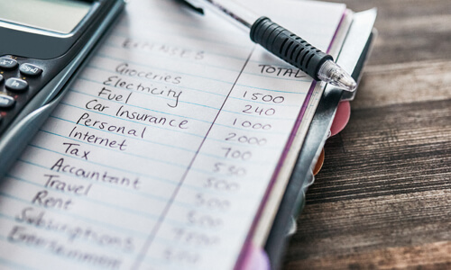 Budget line items written in notebook next to a calculator.