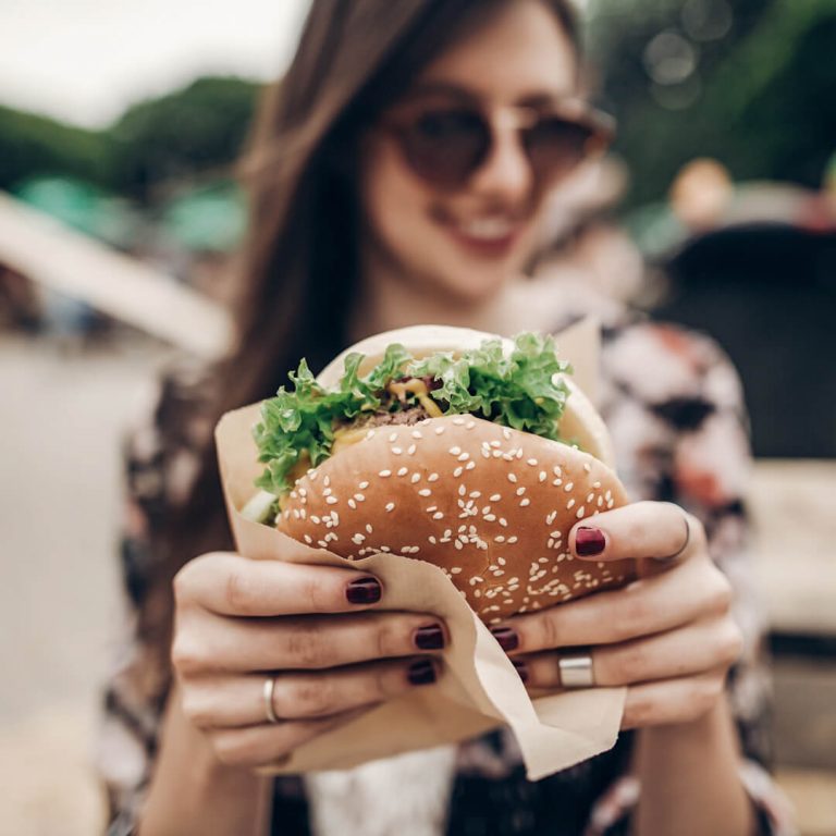 Woman smiling and holding a burger at an outdoor restaurant.
