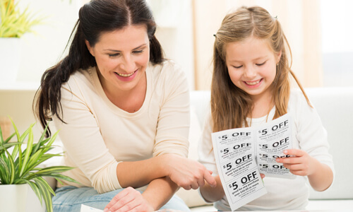 Mother and daughter clipping coupons together, smiling and saving money.