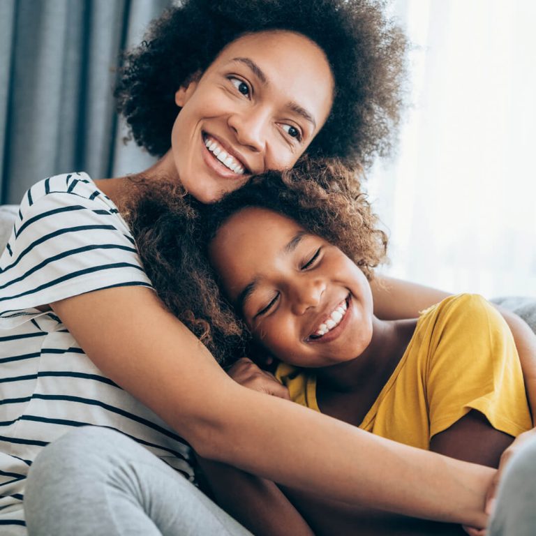 Mother and daughter embrace on couch, smiling.
