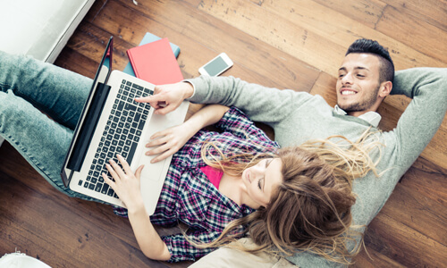 Young couple lying on floor, reviewing their finances on their laptop.
