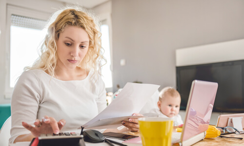 Concerned mother crunching finances with young baby in background.