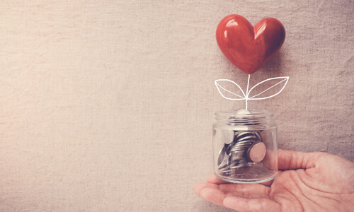 Hand holding jar of coins with heart coming out of jar.