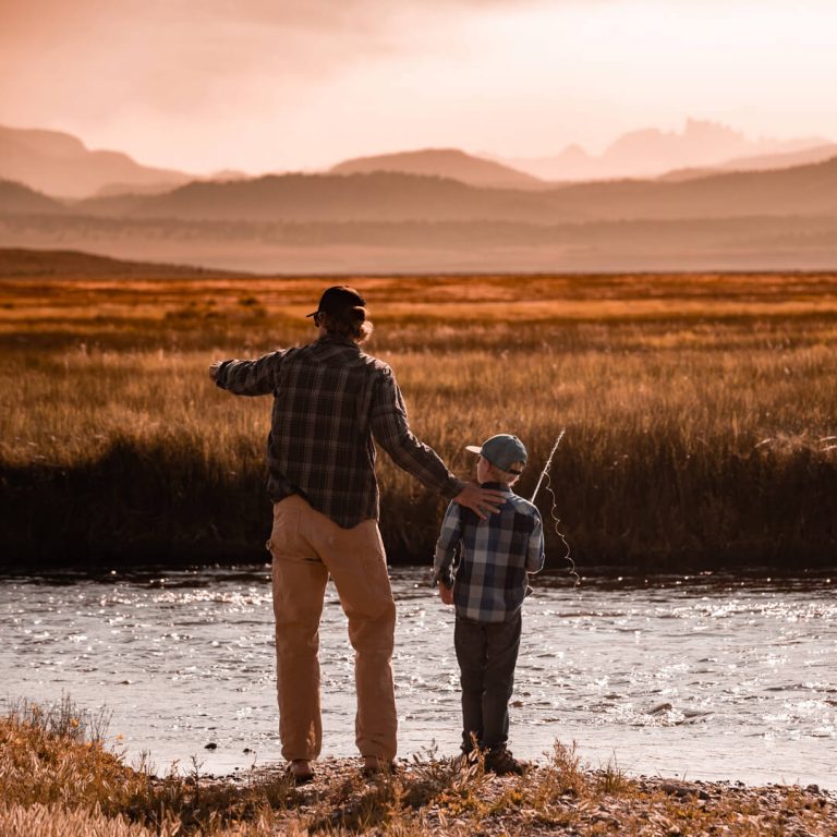 Grandfather and grandson on a grand flyfishing trip. Sunset and mountains in distance.