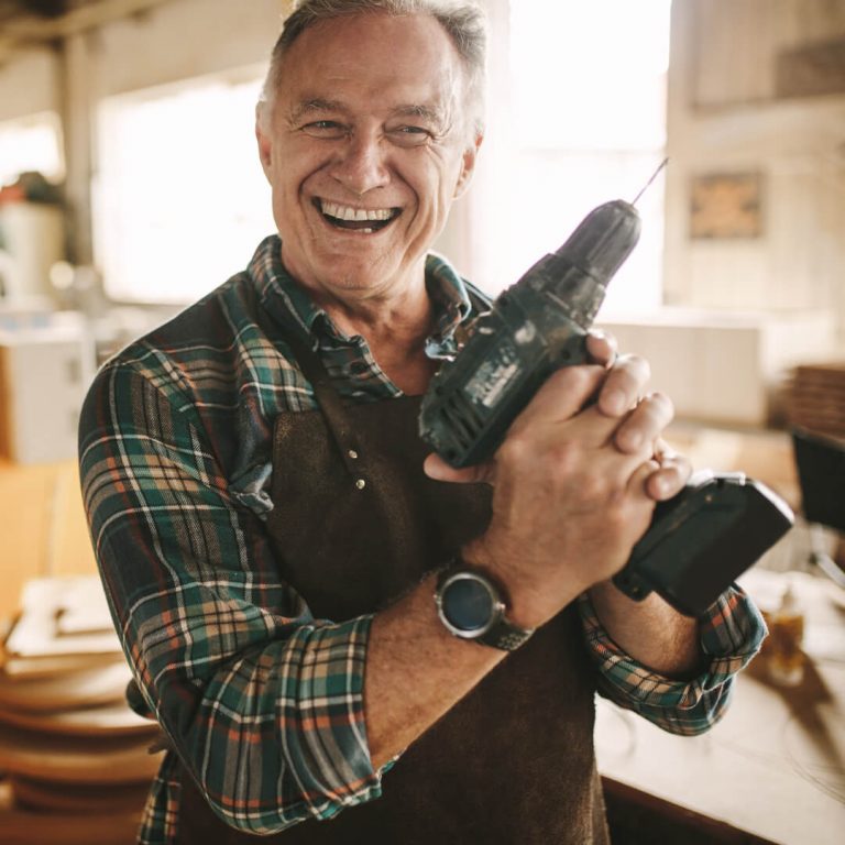 Happy semi-retired man at work in his shop, holding a drill.