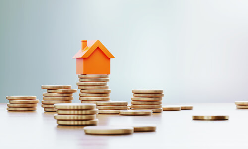 Orange toy house sitting over coin stacks, illustrating the concept of increasing home value.