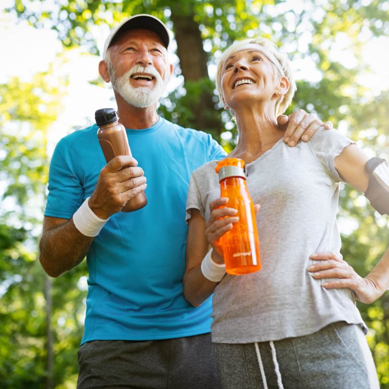 Elderly couple on a healthy walk carrying water bottles, smiling.
