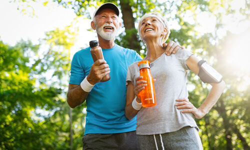 Elderly couple on a healthy walk carrying water bottles, smiling.