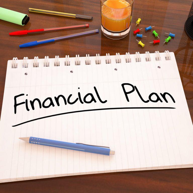 "Financial Plan" written in a notepad on a desk with a calculator and pens.