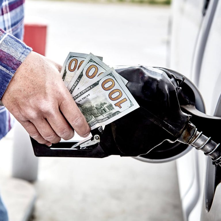 As gas prices rise, a man fills up his car with gasoline and holds three hundred dollar bills.