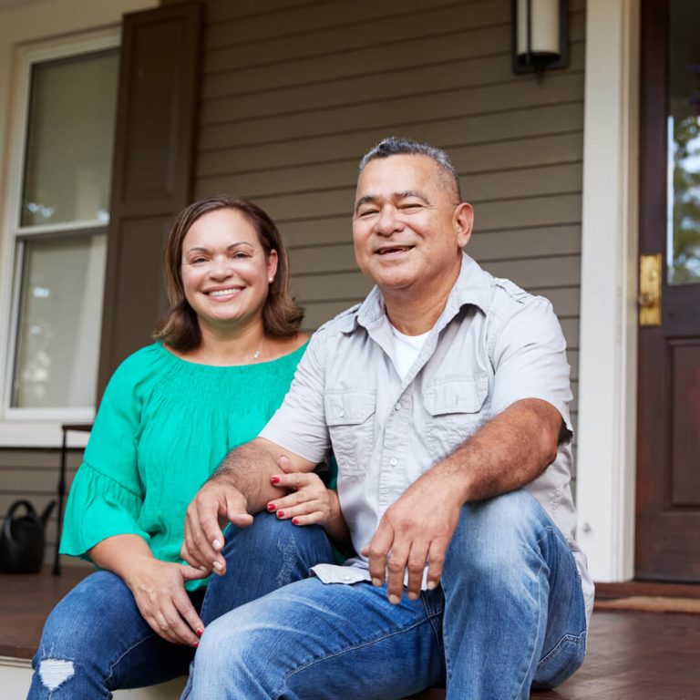 Couple seated on their front porch, smiling.
