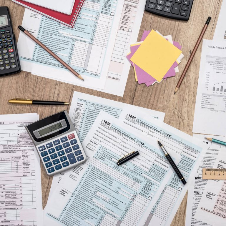 Multiple tax documents on table, with calculator and pens, pencils and ruler.