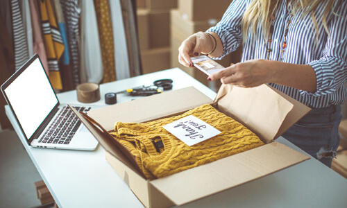 Woman packing up gently-used sweater in a packing box, shipping it to buyer.