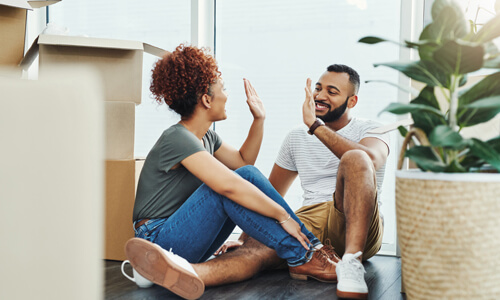 Couple sitting on floor, high-fiving each other, after successfully moving.