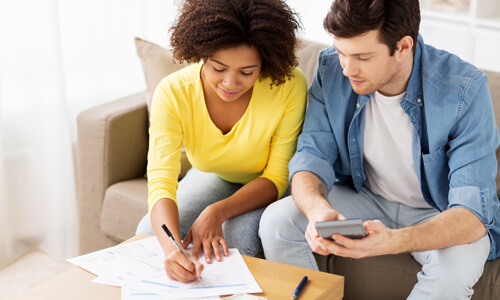 Couple sits on couch reviewing their finances.