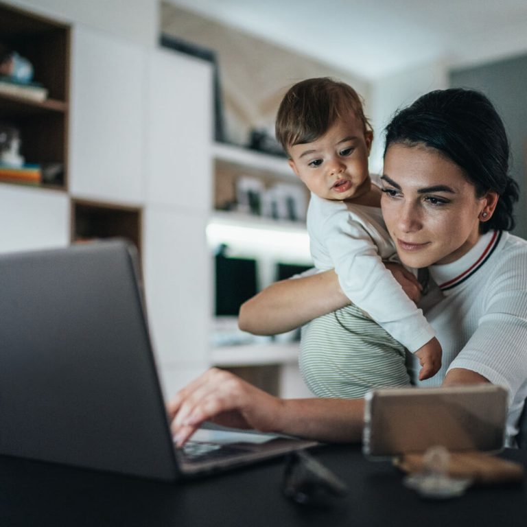 Mother holding young baby looking at computer screen at night.