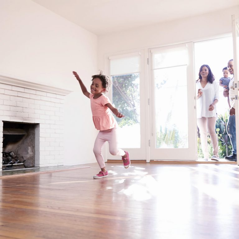 Husband and wife walking into a new home, their child dancing in living room. Made possible by a credit union mortgage.