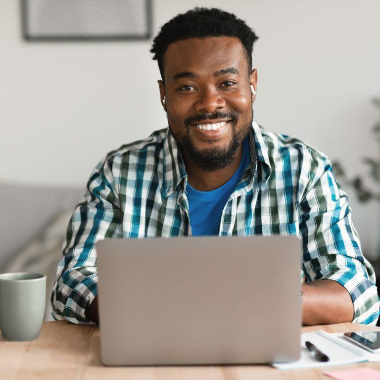 Young smiling man, working from home on his laptop, embracing New Work mentality.