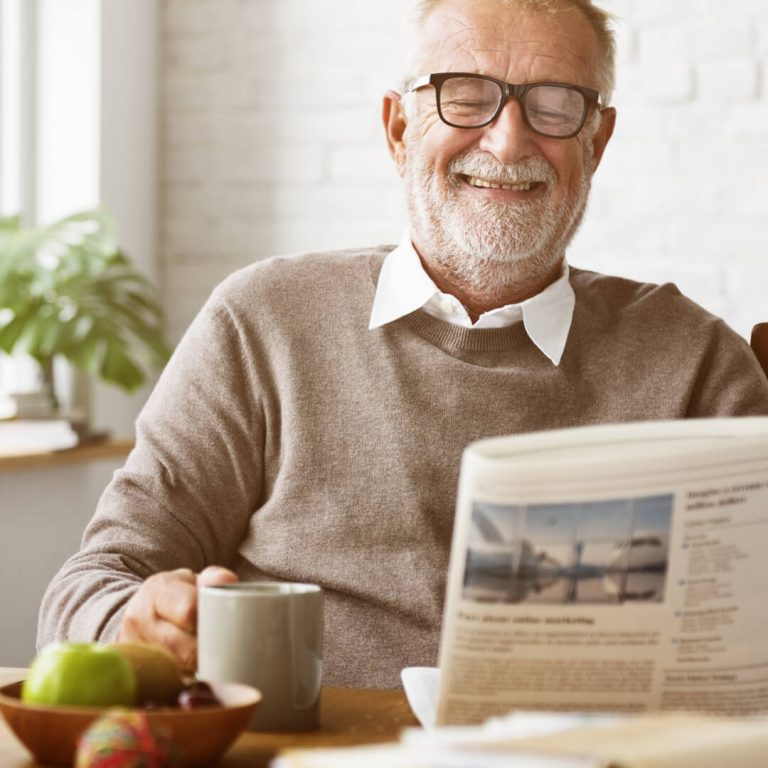Elderly man enjoying retirement alone, smiling, reading newspaper with morning coffee