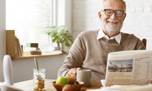 Elderly man enjoying retirement alone, smiling, reading newspaper with morning coffee