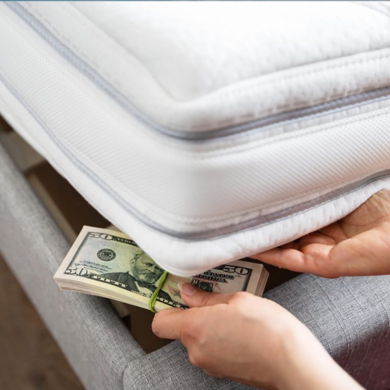 Stack of fifty dollar bills being stashed under mattress.