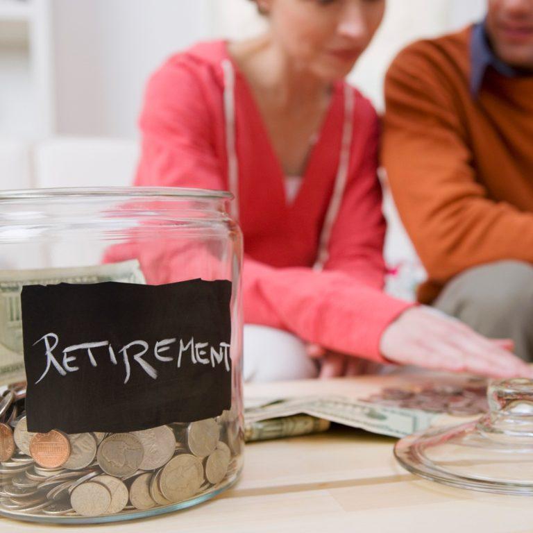 Closeup of change jar labeled "Retirement." Couple in back looking over more coins.
