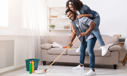Couple in living room mopping floor, spring cleaning.