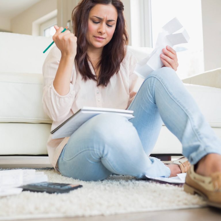 Stressed woman sitting on living room floor, looking at all of her bills.