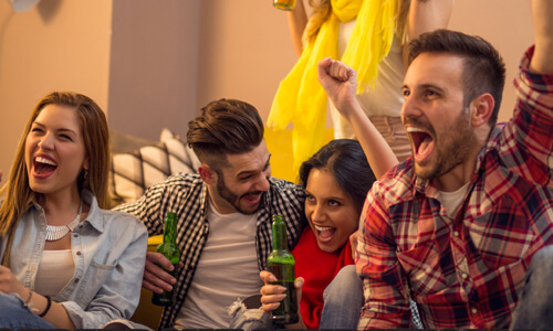 Young group of friends cheers at TV during Super Bowl.