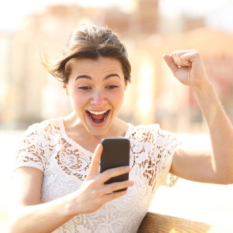 Woman looking at her phone, holding up her hand in excitement after learning her tax refund amount.