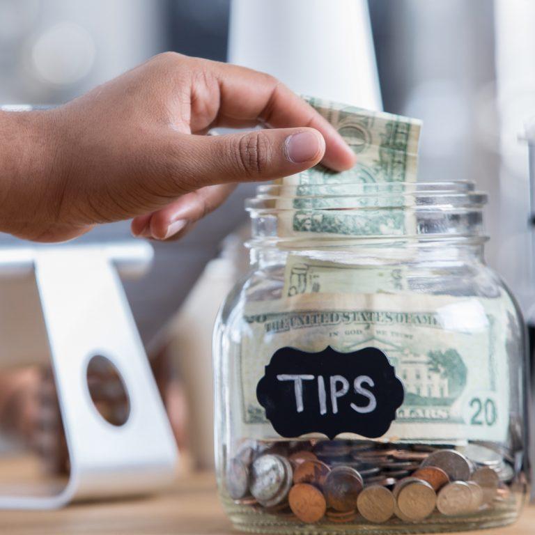 Tip jar with hand dropping a twenty dollar bill into the jar.