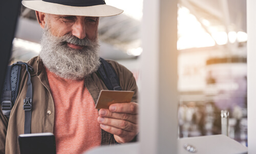 Seasoned traveler calmly looking at his credit card in one hand while dialing a number with his cell phone in the other hand.