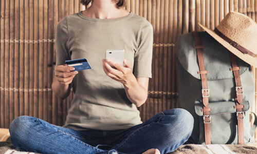 Closeup of woman sitting with a phone and credit card in her hands, planning her next vacation.