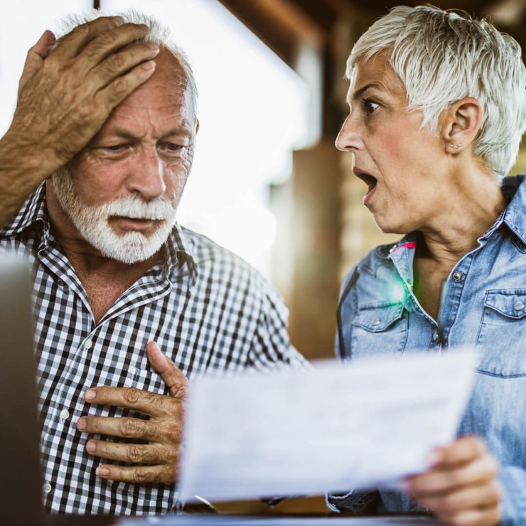 Older man and woman on vacation looking shocked and distress after getting caught in vacation rental scam.