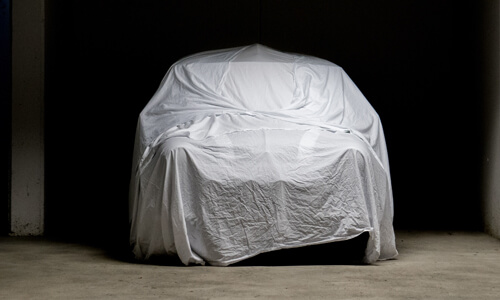 Classic car in garage, under protective cover.