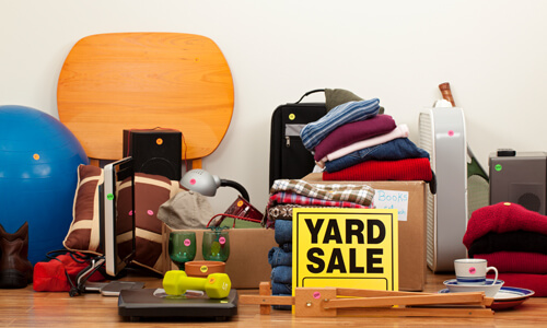 Bunch of used objects in garage with yellow "Yard Sale" sign in front.