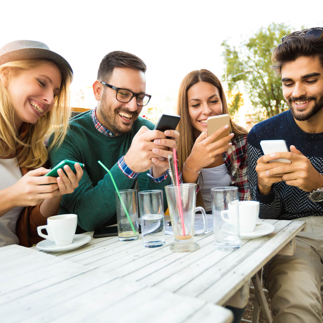Group of friends seated around restaurant table, splitting check with their mobile devices.