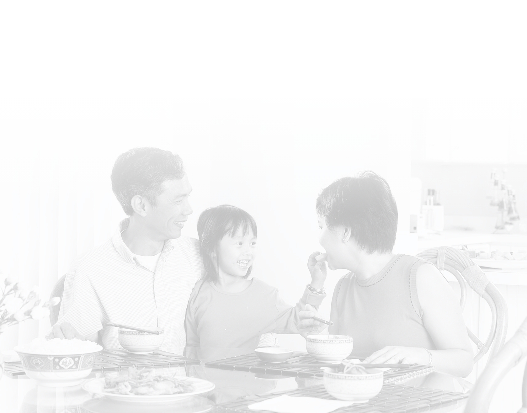 Asian family seated at kitchen table, eating a meal.