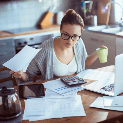 Woman holding a cup of coffee while looking at statements and scheduling online or mobile bill payments.