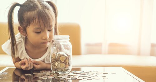 Cute girl looking at her savings jar, waiting for it to grow.