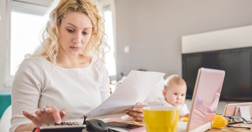 Concerned mother crunching finances with young baby in background.