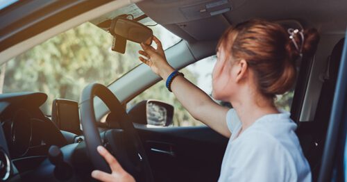 Young woman practicing defensive driving and adjusting her rearview mirror.