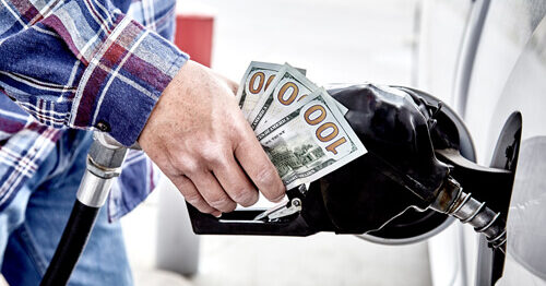 As gas prices rise, a man fills up his car with gasoline and holds three hundred dollar bills.