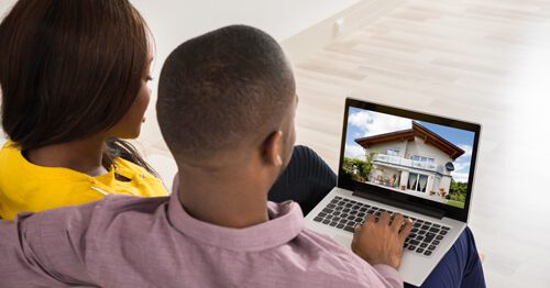 Couple seated on couch looking at new homes on their laptop.